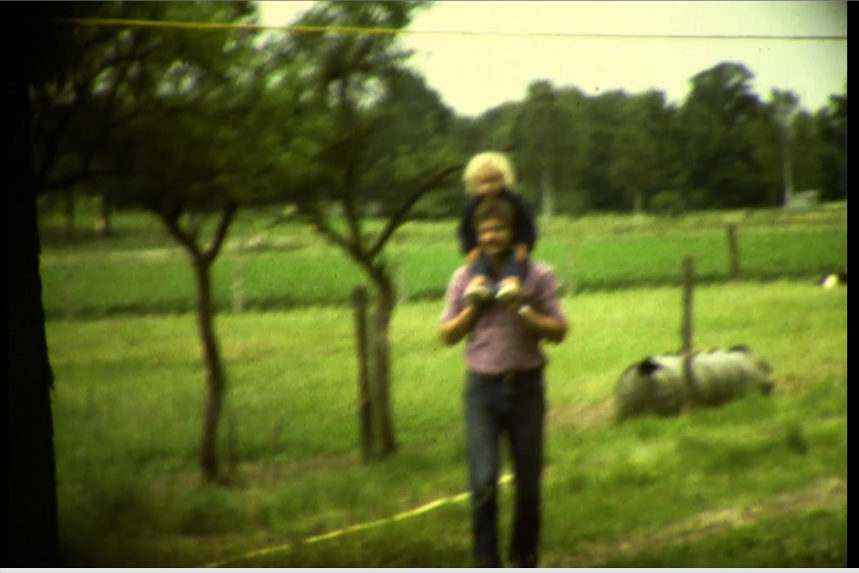 Wiese mit Person, die ein Kind auf den Schultern trägt.