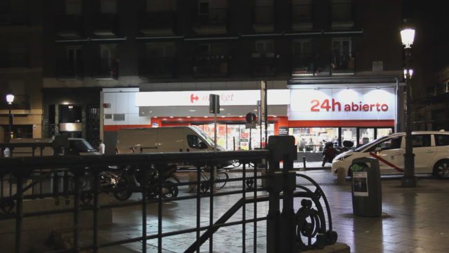 Dunkle Straße mit hellem Schild eines Supermarktes auf dem steht 24h abierto