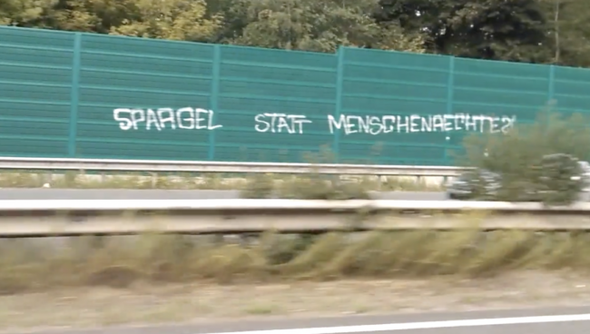 Eine grüne Lärmschutzwand mit der gesprühten Frage: Spargel statt Menschenrechte?