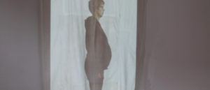 Standbild einer Videoprojektion auf ein Bettlaken in Hochformat einer schwangeren Person