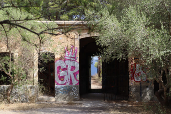 Verfallenes Gebäude mit Graffitti und hineinragenden Ästen durch eine Türöffnung ist das Meer in der Ferne zu sehen